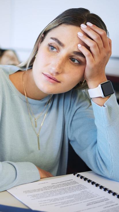 Een student zit na te denken in de collegezaal en staart voor zich uit