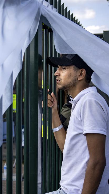 vluchteling kijkt uitzichtloos naar buiten door het hek