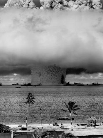 een zwart-witfoto van een grote test met een atoombom bij een tropisch eiland in de buurt, je ziet een enorme wolk boven het water