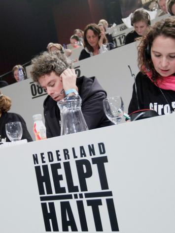vrijwilligers van Giro555 nemen telefoontjes op, met daarvoor de grote tekst 'Nederland helpt Haïti'
