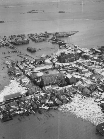 een zwart-witfoto van een overstroomd dorp tijdens de Watersnoodramp, vanuit een vliegtuig genomen