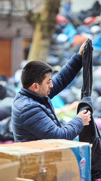 Man zoekt kleding uit tussen een vuilnisbelt vol met dozen en zakken met andere kleding