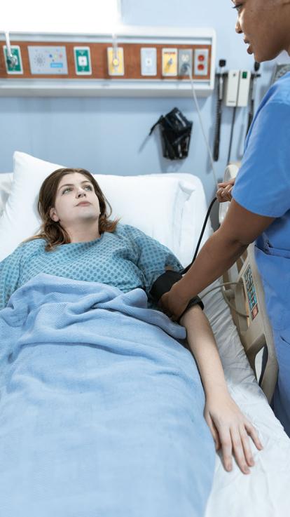 Vrouw ligt in ziekenhuisbed in operatiejasje terwijl verpleegkundige haar bloeddruk meet