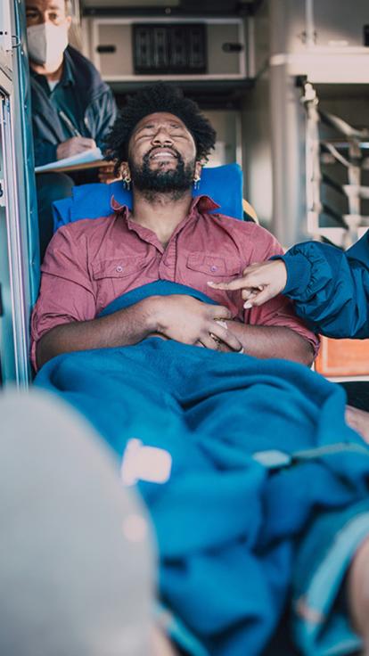 Man ligt in ambulance en knijpt ogen dicht van de pijn 