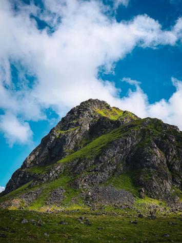 een heuvel van steen en groen met een achtergrond van blauwe lucht en wolken