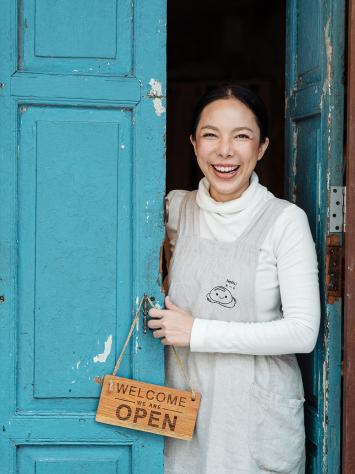 een vrouw opent lachend de deur en hangt een 'welkom'-bordje op