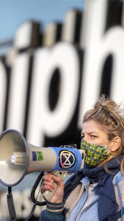 Iemand met een megafoon, waarop het logo van Extinction Rebellion te zien is. 