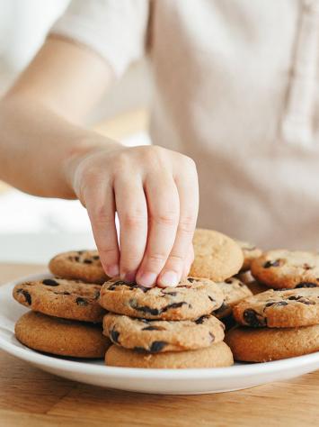 een hand pakt een koekje van een bord met koekjes af 