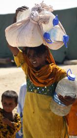 Pakistaans meisje tilt zware flessen water op haar hoofd. 