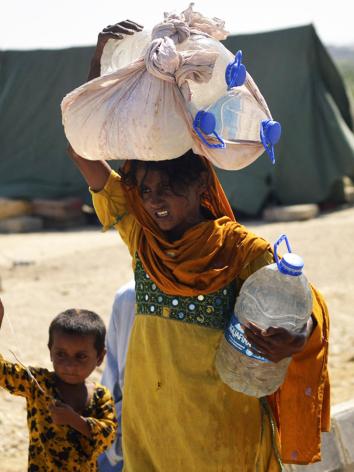 Pakistaans meisje tilt zware flessen water op haar hoofd. 