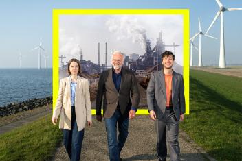 Foto presentatoren van de serie: Wat houdt ons Tegen? lopend in weiland met windmolens en fabriek om zich heen