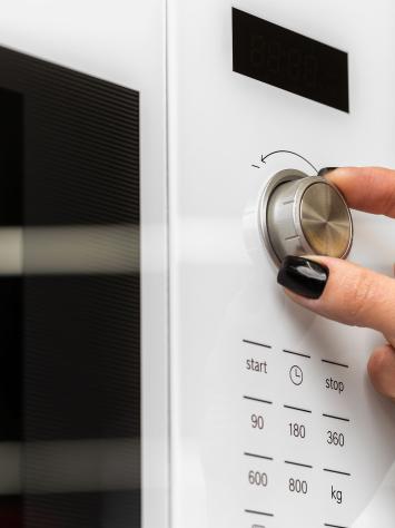 Handen met lange nagels draaien aan knop magnetron