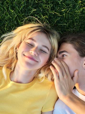 Jongen en meisje liggen blij in gras en fluisteren in elkaars oor