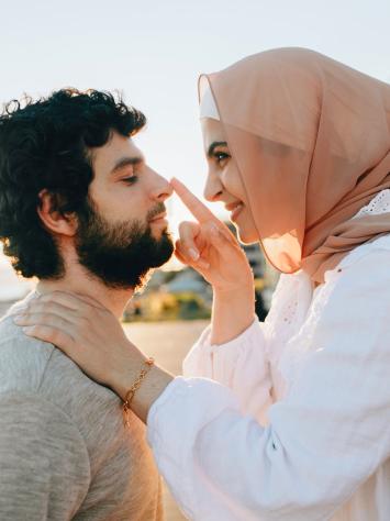 Vrouw met hoofddoek kijkt speels en verliefd naar man. 