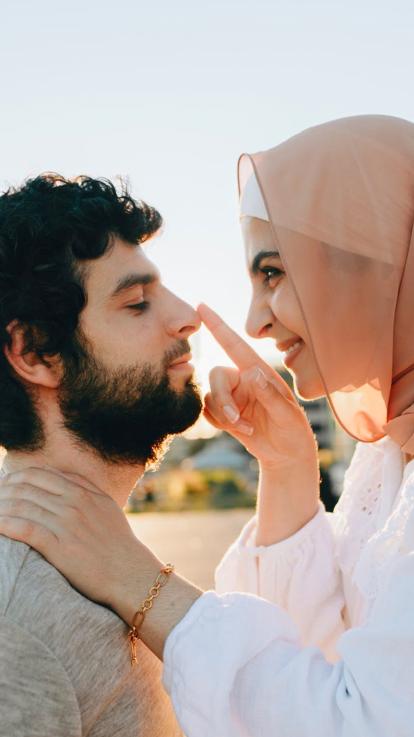 Vrouw met hoofddoek kijkt speels en verliefd naar man. 