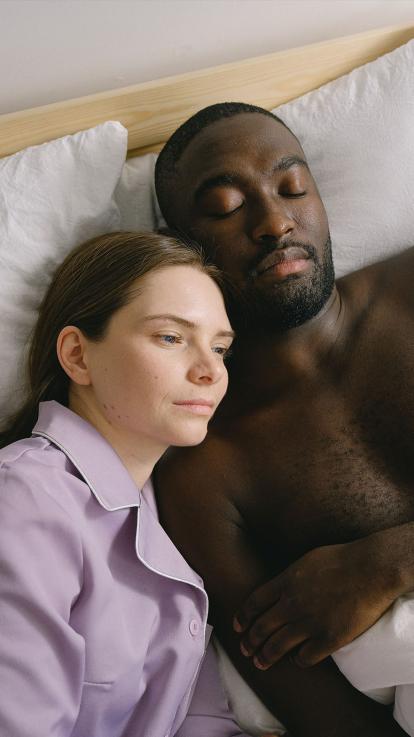 Vrouw ligt met man in bed, dromerig voor zich uit te kijken. 