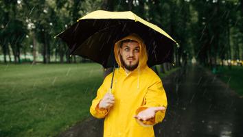 iemand staat met regenjas en paraplu in de regen