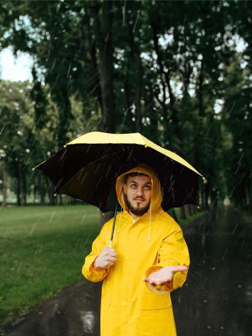 iemand staat met regenjas en paraplu in de regen