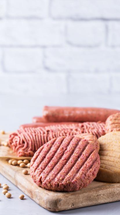 Je ziet op een smijplank verschillende soorten vleesvervangers, een burger, worst en gehakt.