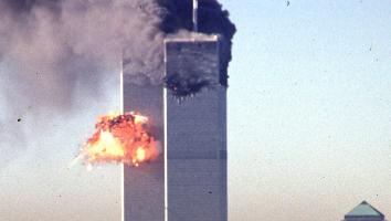 Een foto van de Twin Towers in 2001, direct na de tweede aanslag. Midden op de linkertoren is een vuurexplosie te zien. De rechtertoren staat in brand met dikke zwarte rookwolken.