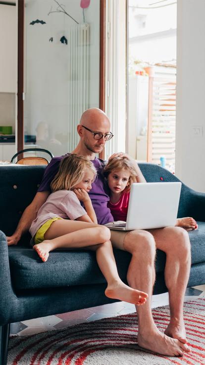 Vader kijkt met twee kinderen naar serie op laptop op de bank. 