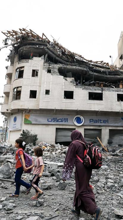 Een vrouw en twee jonge kinderen lopen over het puin in Gaza, dat gebombardeerd is. 