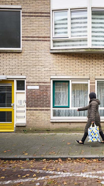 Mevrouw loopt met een boodschappentasje op straat in een wijk met sociale huurwoningen