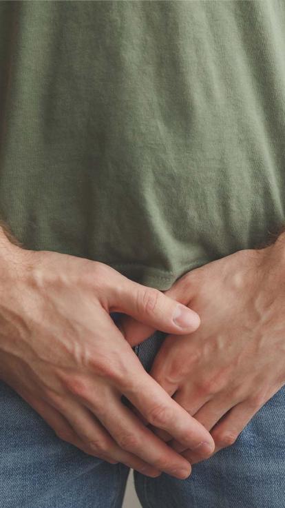 Man houdt handen voor zijn zijn kruis.