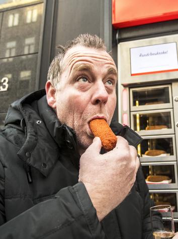 Iemand bij een snackautomaat die een kroket eet. 