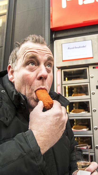 Iemand bij een snackautomaat die een kroket eet. 
