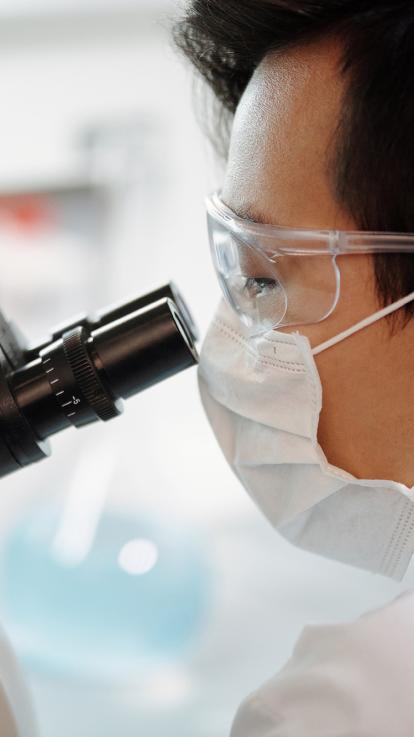 een laborant kijkt door een microscoop