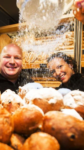 Poedersuiker wordt gestrooid over een bak met knapperige en sappige oliebollen. 