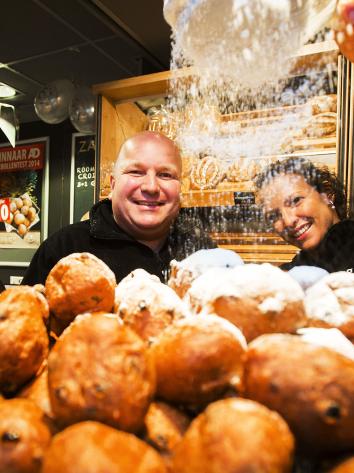 Poedersuiker wordt gestrooid over een bak met knapperige en sappige oliebollen. 