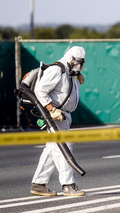 Meneer in veiligheidskleding loopt tijdens asbest opruiming op de A1 met een bladblazer