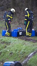 Twee mannen in uniform buigen over jerycans met chemisch afval in bos