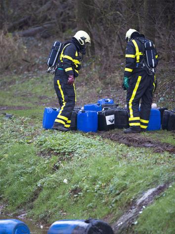 Twee mannen in uniform buigen over jerycans met chemisch afval in bos