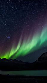 het felgroene noorderlicht in een donkere lucht boven gebergte