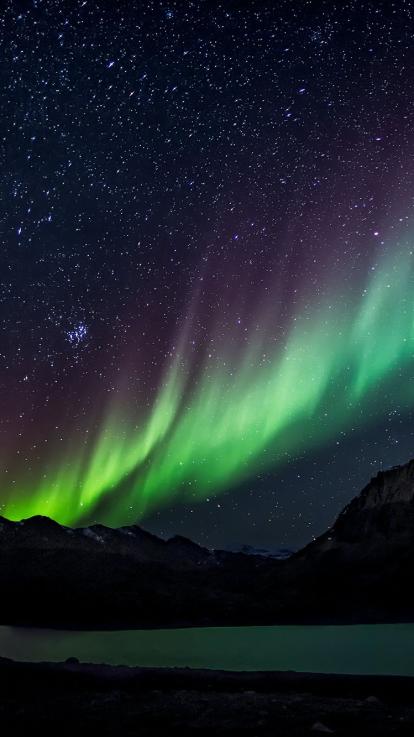 het felgroene noorderlicht in een donkere lucht boven gebergte