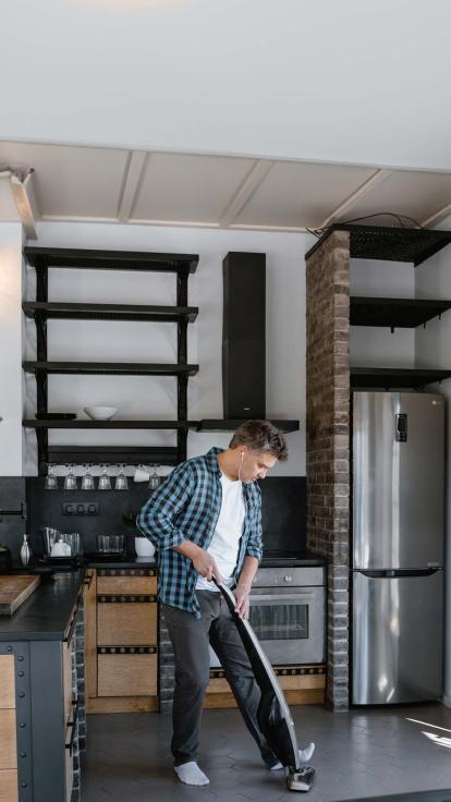 Man stofzuigt een industriële keuken met oortjes in.