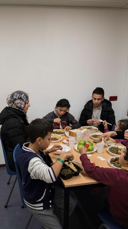 Een familie eet samen aan tafel in azc. 