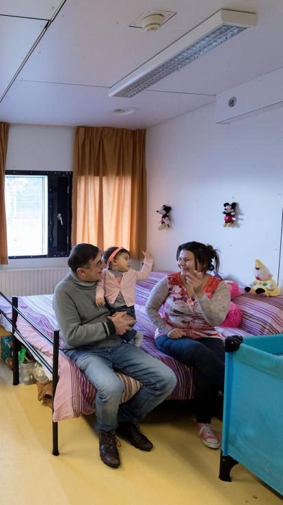 Een gezin zit op bed in hun slaapkamer in het azc.