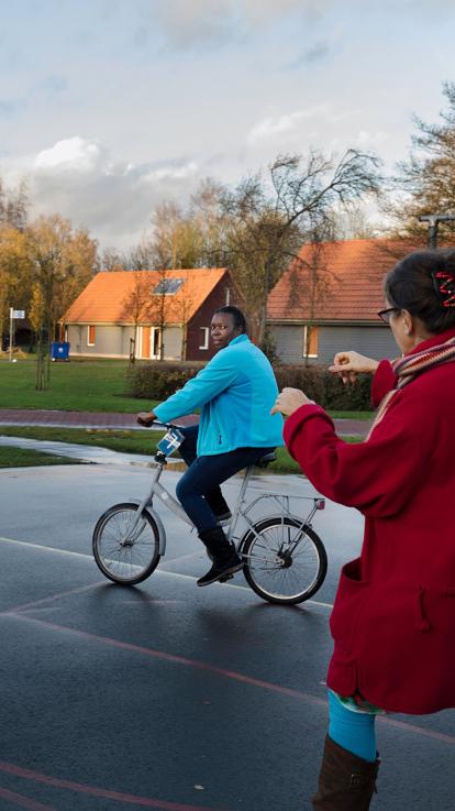 Vrouw leert fietsen op een basketbalveldje.