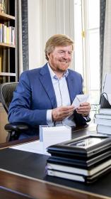 De koning zit achter zijn bureau met een envelop in zijn hand.