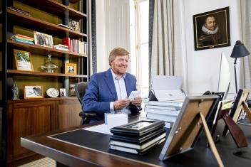 De koning zit achter zijn bureau met een envelop in zijn hand.