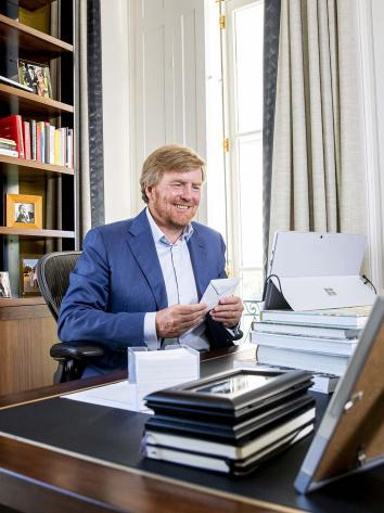 De koning zit achter zijn bureau met een envelop in zijn hand.