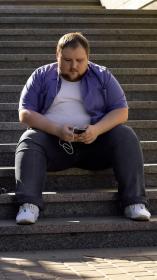 een man met obesitas zit op een trap naar muziek te luisteren