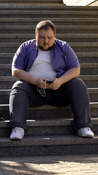 een man met obesitas zit op een trap naar muziek te luisteren