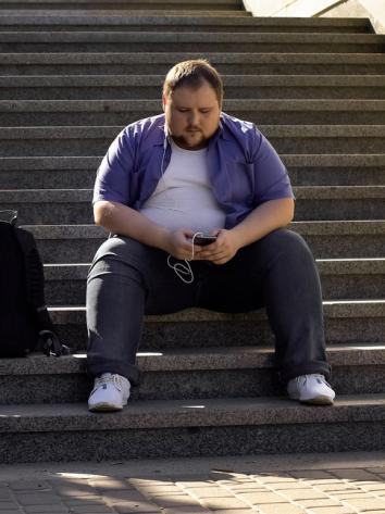 een man met obesitas zit op een trap naar muziek te luisteren