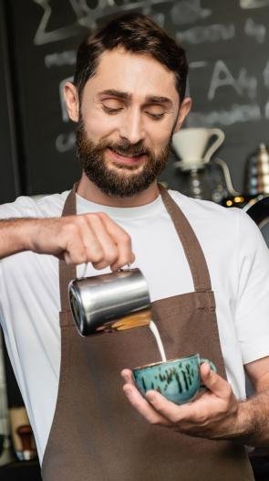 Man schenkt melk in kopje koffie in een café. 