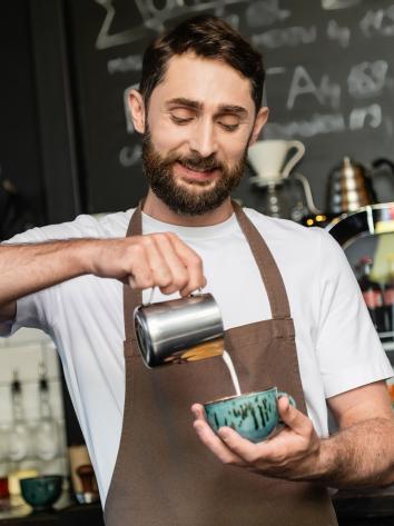 Man schenkt melk in kopje koffie in een café. 